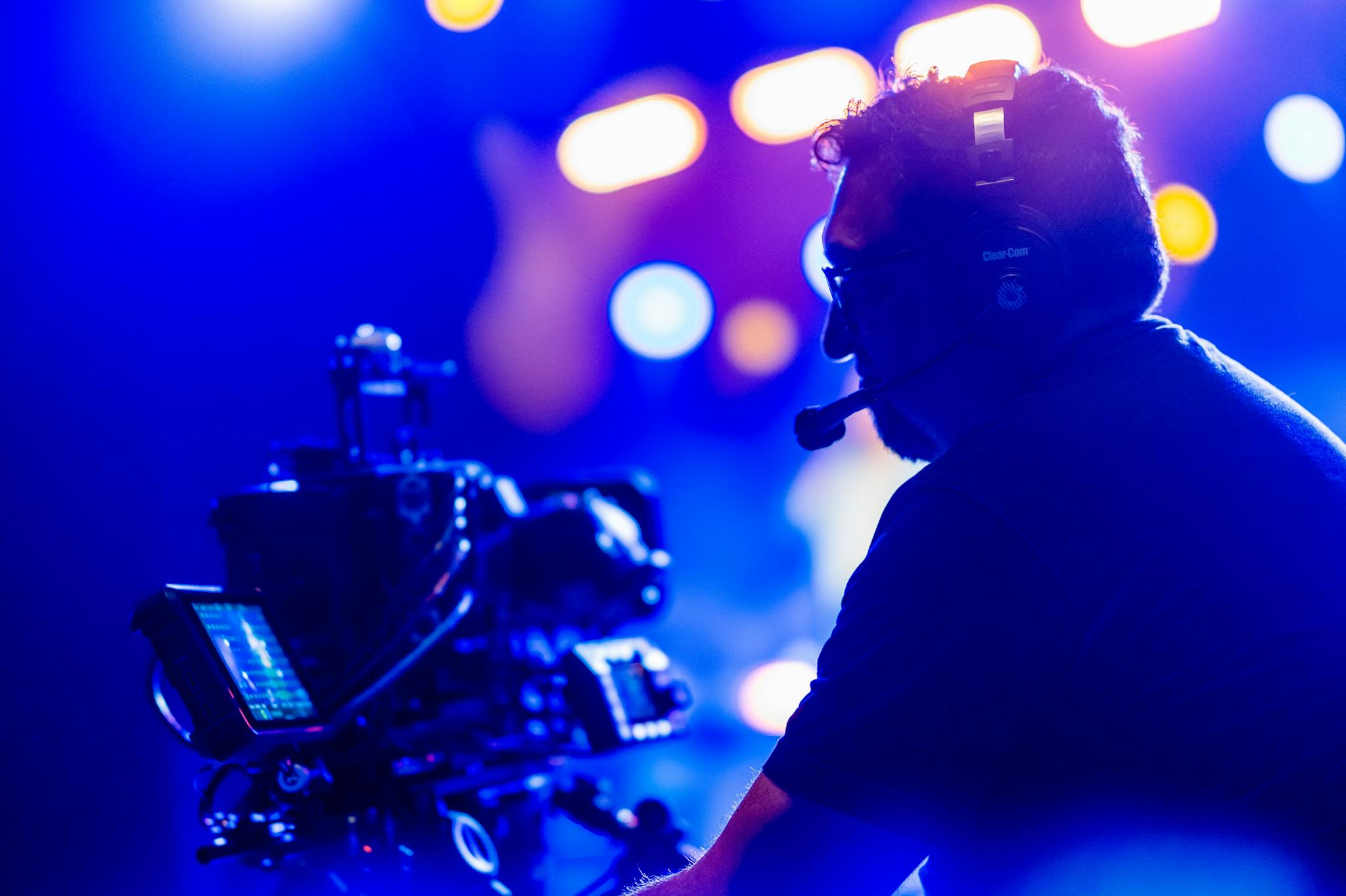 Cameraman operating equipment during a vibrant night event with colorful lights.