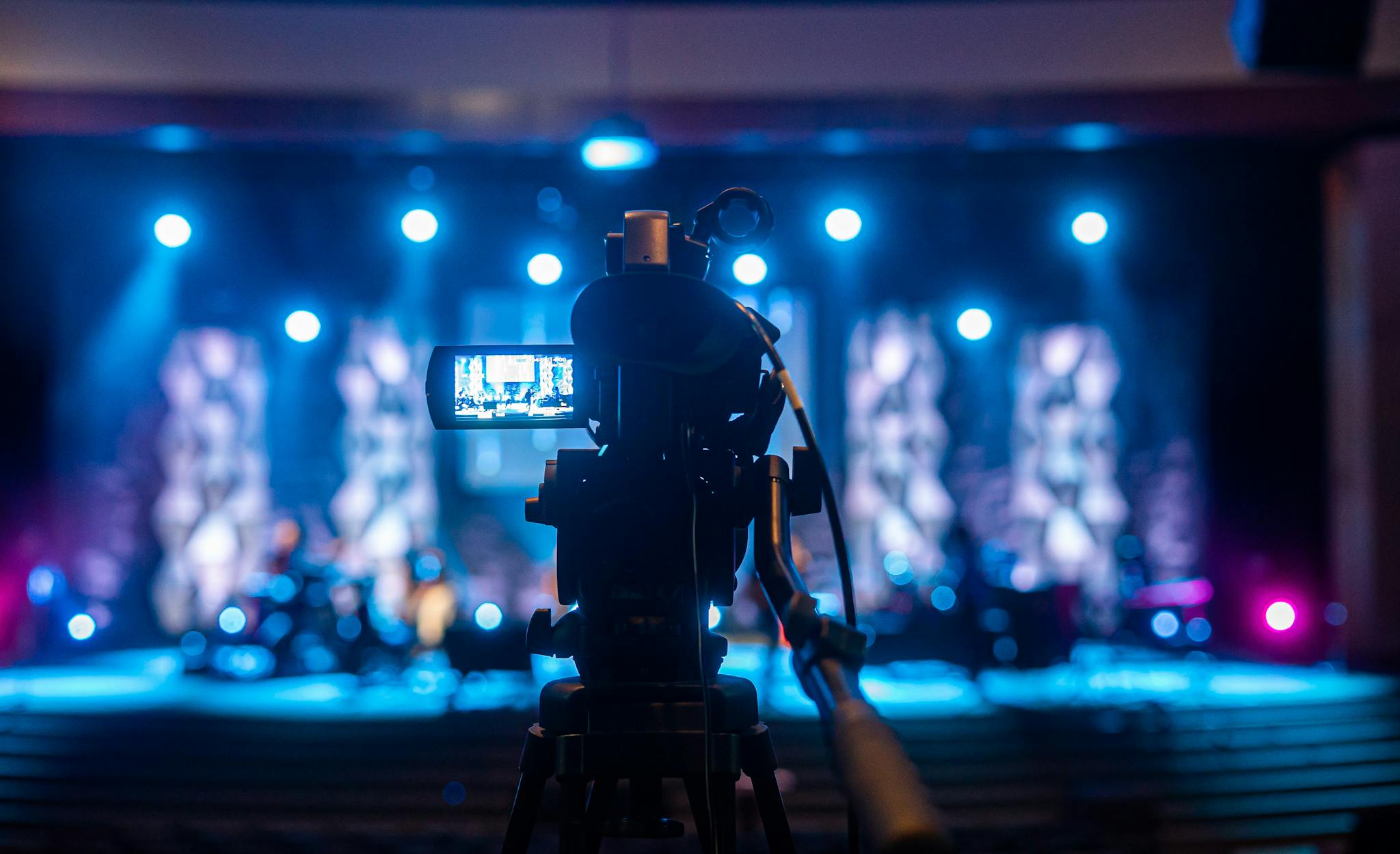 Video camera capturing a vibrant concert scene under bright stage lights.